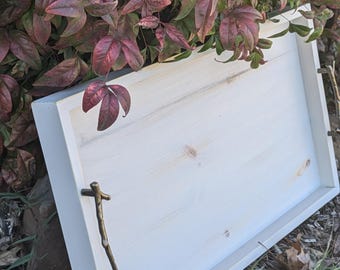 May include: White wooden serving tray with two gold metal twig handles. The tray is sitting on a bed of brown leaves.