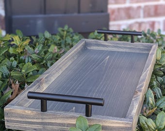 May include: A gray wooden serving tray with black metal handles. The tray is sitting on a bed of green leaves.