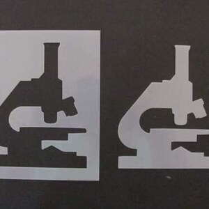 May include: Two microscope stencils, one black and one white, on a black background.