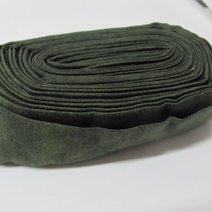 May include: A roll of dark green fabric, tightly wound into a coil. The fabric has a slightly textured surface.