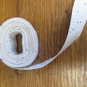 May include: A roll of white fabric with small blue polka dots. The fabric is rolled up and tied with a white ribbon.