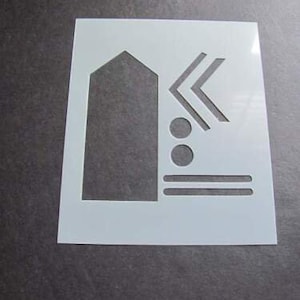 May include: White plastic stencil with a geometric design. The stencil features a rectangle, two circles, two lines, and a chevron shape.
