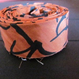 May include: A roll of orange fabric with a black abstract pattern. The fabric is rolled up tightly and the ends are visible.