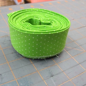 May include: A roll of green fabric with white polka dots. The fabric is rolled up tightly and is sitting on a gray cutting mat.