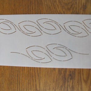 May include: White plastic quilting stencil with a repeating pattern of curved leaf shapes. The stencil is labeled "Oval Leaf Border".