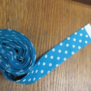 May include: A roll of teal blue fabric with white polka dots. The fabric is rolled up and the end is unrolled, showing the pattern.