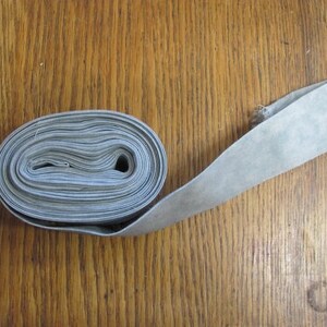 May include: A roll of light gray fabric ribbon, wound into a coil, with one end extending out.