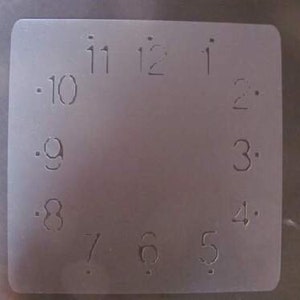May include: A white plastic clock face stencil with numbers 1 through 12 and 10 through 2.
