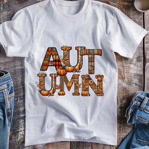 Pode incluir: Camiseta branca com a palavra "AUTUMN" escrita em letras grandes e coloridas. As letras s&atilde;o feitas de um mosaico de diferentes tecidos, incluindo padr&otilde;es de xadrez, flores e paisley. As letras s&atilde;o decoradas com pequenas ab&oacute;boras, folhas e bolotas.