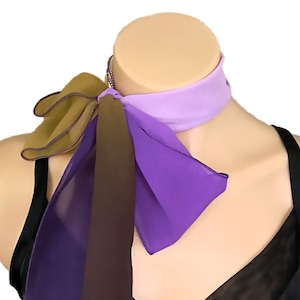May include: A colorful scarf with a lavender neckband and cascading purple and brown fabric. The scarf is draped on a mannequin, showcasing its design and texture. The scarf is paired with a black top.
