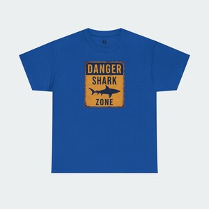 A blue t-shirt with a graphic design that says "DANGER SHARK ZONE" in bold letters.