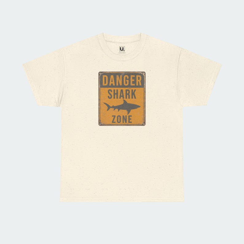 A white t-shirt with a graphic design featuring a warning sign that says "DANGER SHARK ZONE".