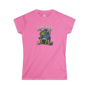 Peut inclure: Un t-shirt rose vif à manches courtes orné d'un motif représentant une grenouille verte en sweat à capuche bleu, assise dans un fauteuil de jeu avec une manette. Le texte GAME OVER est imprimé au-dessus, avec une icône de batterie faible.
