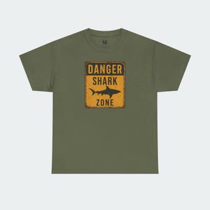 A green t-shirt with a graphic design that says "DANGER SHARK ZONE" in bold letters.
