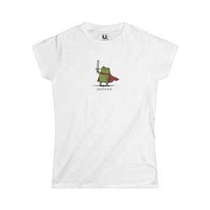 Op de afbeelding: Een wit t-shirt met korte mouwen en een centrale afbeelding van een groene kikker die een rode cape draagt en een klein zilveren zwaard vasthoudt. Onder de kikker staat het woord HUZZAH in zwarte hoofdletters gedrukt.