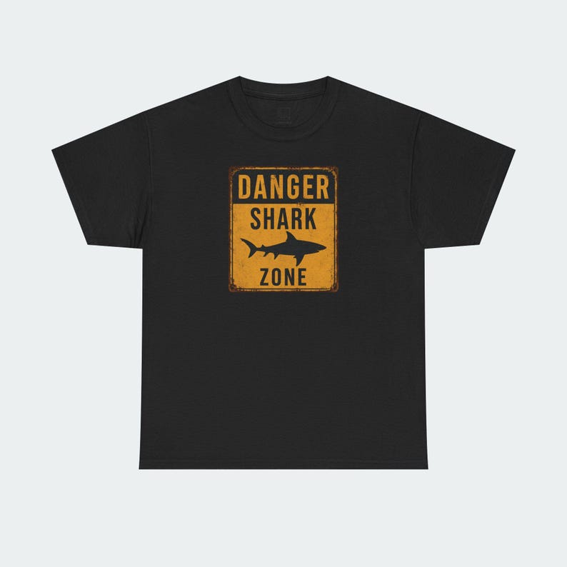 A black t-shirt with a graphic design featuring a shark silhouette and the text "DANGER SHARK ZONE" printed on it.