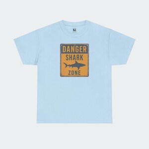 A light blue t-shirt with a graphic design featuring a shark and the text "DANGER SHARK ZONE" printed on it.