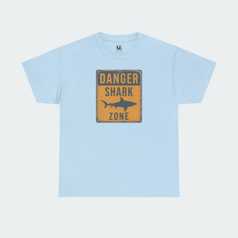 A light blue t-shirt with a graphic design featuring a shark and the text "DANGER SHARK ZONE" printed on it.