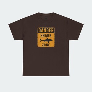 A brown t-shirt with a graphic design that says "DANGER SHARK ZONE" in bold letters.