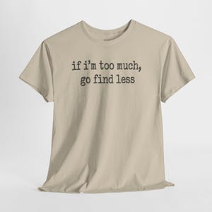 A beige t-shirt with the text "if I'M TOO MUCH, go find less" printed on it.