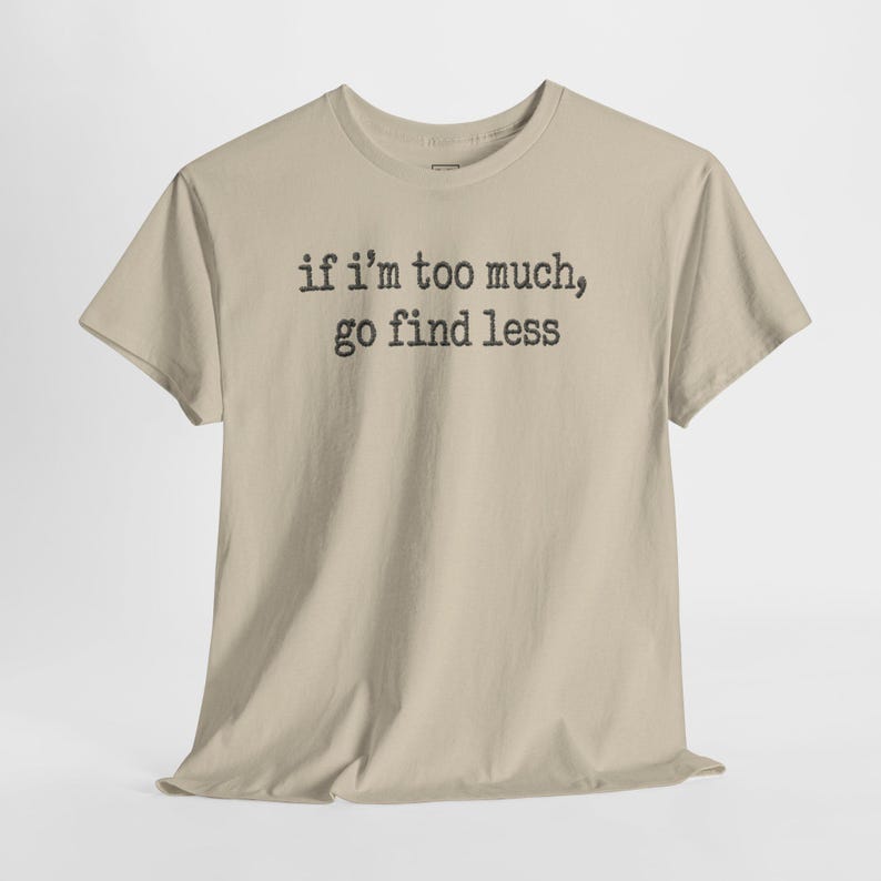 A beige t-shirt with the text "if I'M TOO MUCH, go find less" printed on it.