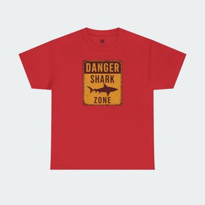 A red t-shirt with a graphic design that says "DANGER SHARK ZONE" in bold letters.