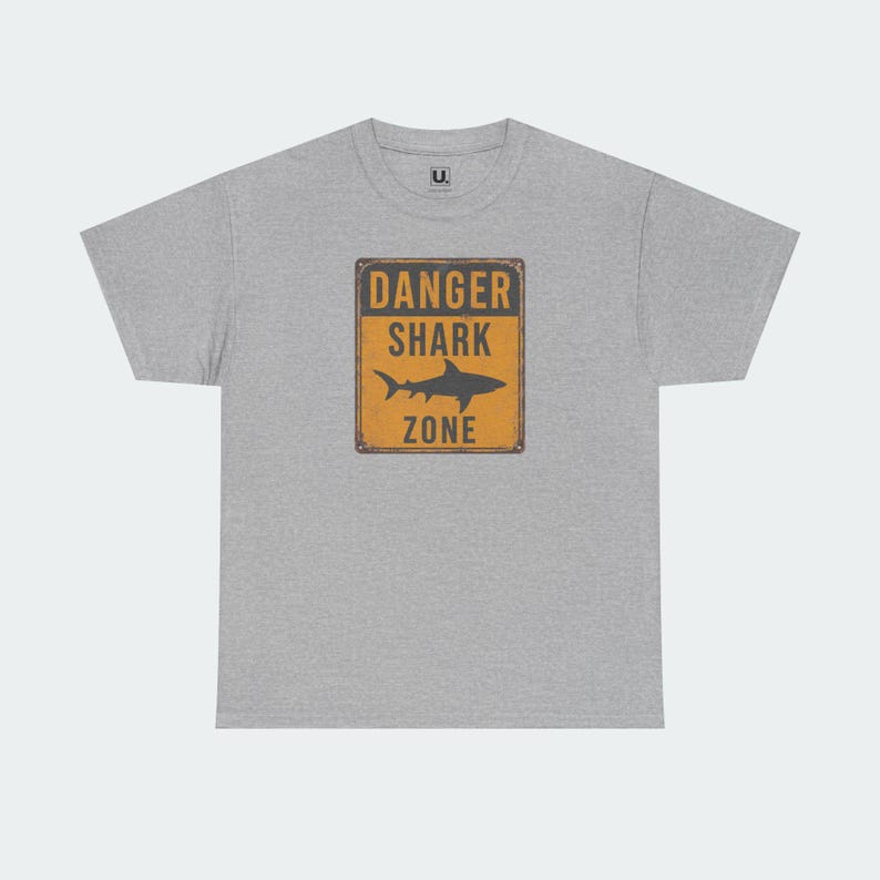 A gray t-shirt with a graphic design featuring a shark and the text "DANGER SHARK ZONE" printed on it.