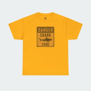 A yellow t-shirt with a graphic design that says "DANGER SHARK ZONE" in bold letters.