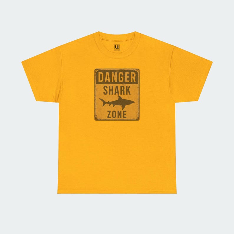 A yellow t-shirt with a graphic design that says "DANGER SHARK ZONE" in bold letters.
