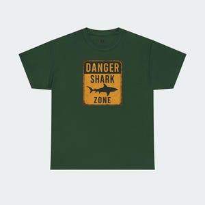 A green t-shirt with a graphic design that says "DANGER SHARK ZONE" in bold letters.