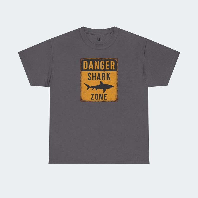 A gray t-shirt with a graphic design featuring a shark silhouette and the text "DANGER SHARK ZONE" printed on it.