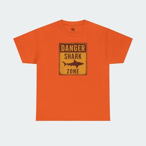 An orange t-shirt with a graphic design that says "DANGER SHARK ZONE" in bold letters.