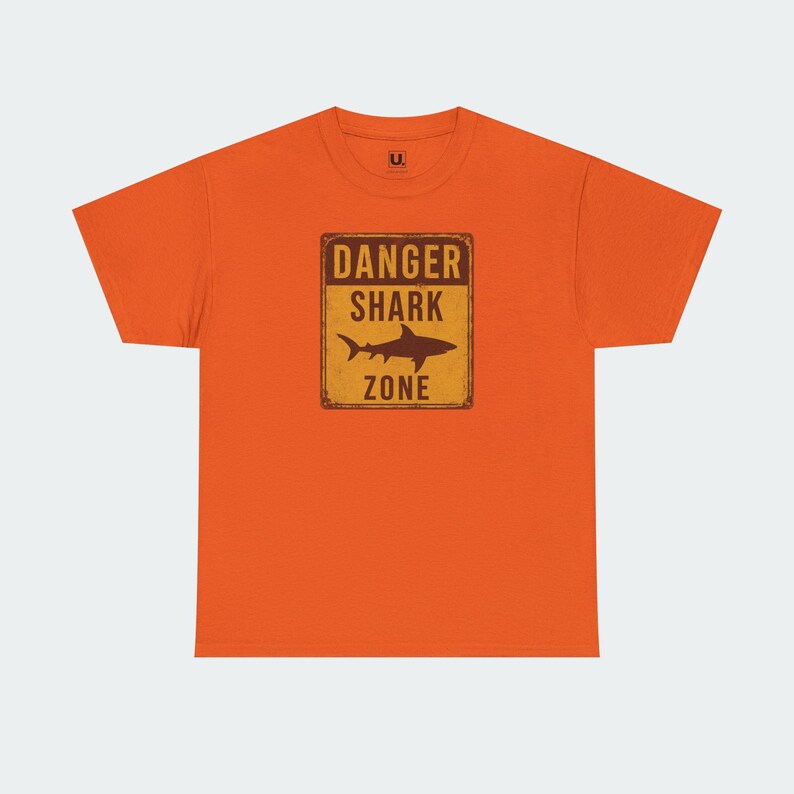 An orange t-shirt with a graphic design that says "DANGER SHARK ZONE" in bold letters.