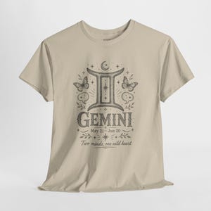 May include: A beige short-sleeve t-shirt featuring a black ink-style graphic of the Gemini zodiac symbol, butterflies, stars, and the text: GEMINI, May 21 - Jun 20, Two minds, one wild heart. The design is centered on the front of the crew neck shirt.