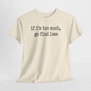 A cream-colored t-shirt with the text "if I'M TOO MUCH, go find less" printed on it.