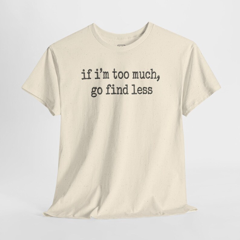 A cream-colored t-shirt with the text "if I'M TOO MUCH, go find less" printed on it.