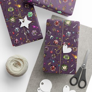 May include: Three wrapped gifts with purple paper featuring a fantasy-themed pattern of dice, potions, and weapons. Each gift is tied with twine and a white tag. A ball of twine, scissors, and blank tags are also present.