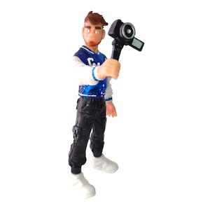 May include: A blue and white varsity jacket with a blue and white striped collar and a black and white camera. The figure is wearing black pants and white sneakers.