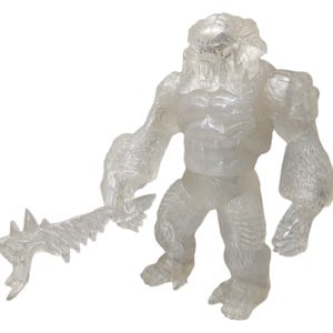 Puede incluir: Una figura de acción translúcida blanca de un monstruo sosteniendo un arma. La figura está hecha de un material plástico transparente y tiene un diseño detallado.