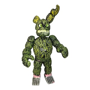 Könnte beinhalten: Eine grüne und gelbe Actionfigur eines Charakters mit einem hasenartigen Ohr. Die Figur hat ein strukturiertes, moosiges Aussehen mit sichtbaren Details wie einem skelettartigen Mund und grünen Augen. Die Füße der Figur haben rosa Akzente.