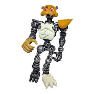 Puede incluir: Un juguete robot de color plateado y negro con una cabeza amarilla y una pajarita blanca. El robot tiene un rayo en el pecho y está en posición con los brazos extendidos.