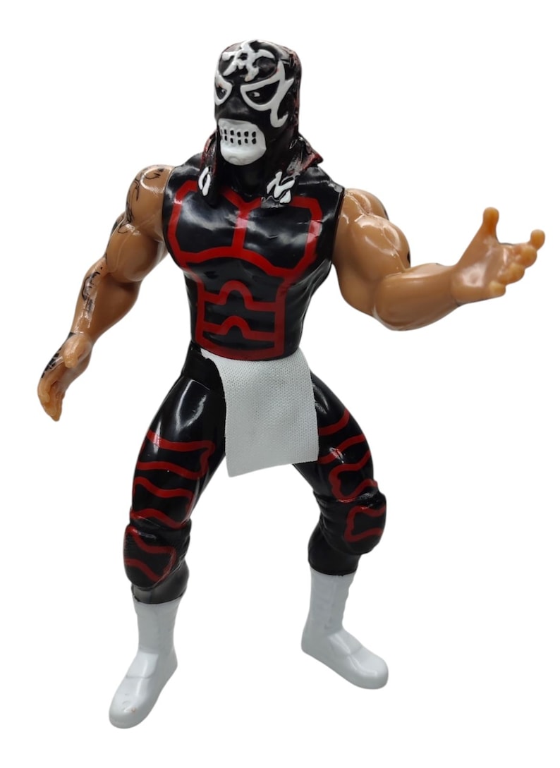 Puede incluir: Figura de acci&oacute;n negra y roja de un luchador enmascarado. La figura tiene una m&aacute;scara negra con detalles blancos, un atuendo negro y rojo y botas blancas. La figura posa con un brazo levantado.