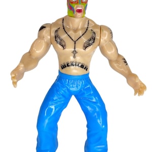 May include: A plastic action figure of a wrestler wearing a yellow, red, and blue mask with a black and white tattoo on his chest. The figure is wearing blue pants and has a black necklace with a cross pendant.
