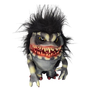 Puede incluir: Una figura de criatura grotesca con una expresión amenazante. Tiene una boca grande llena de dientes afilados, ojos amarillos y pelo negro puntiagudo. El cuerpo es gris con rayas amarillas y detalles rojos en los pies.