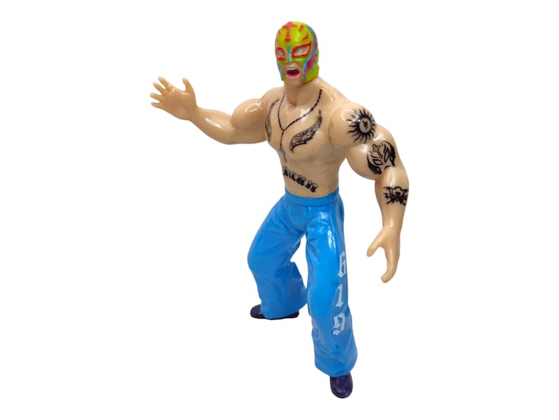 May include: A wrestler action figure with a colorful mask, tattoos, and blue pants with white lettering that says "619".