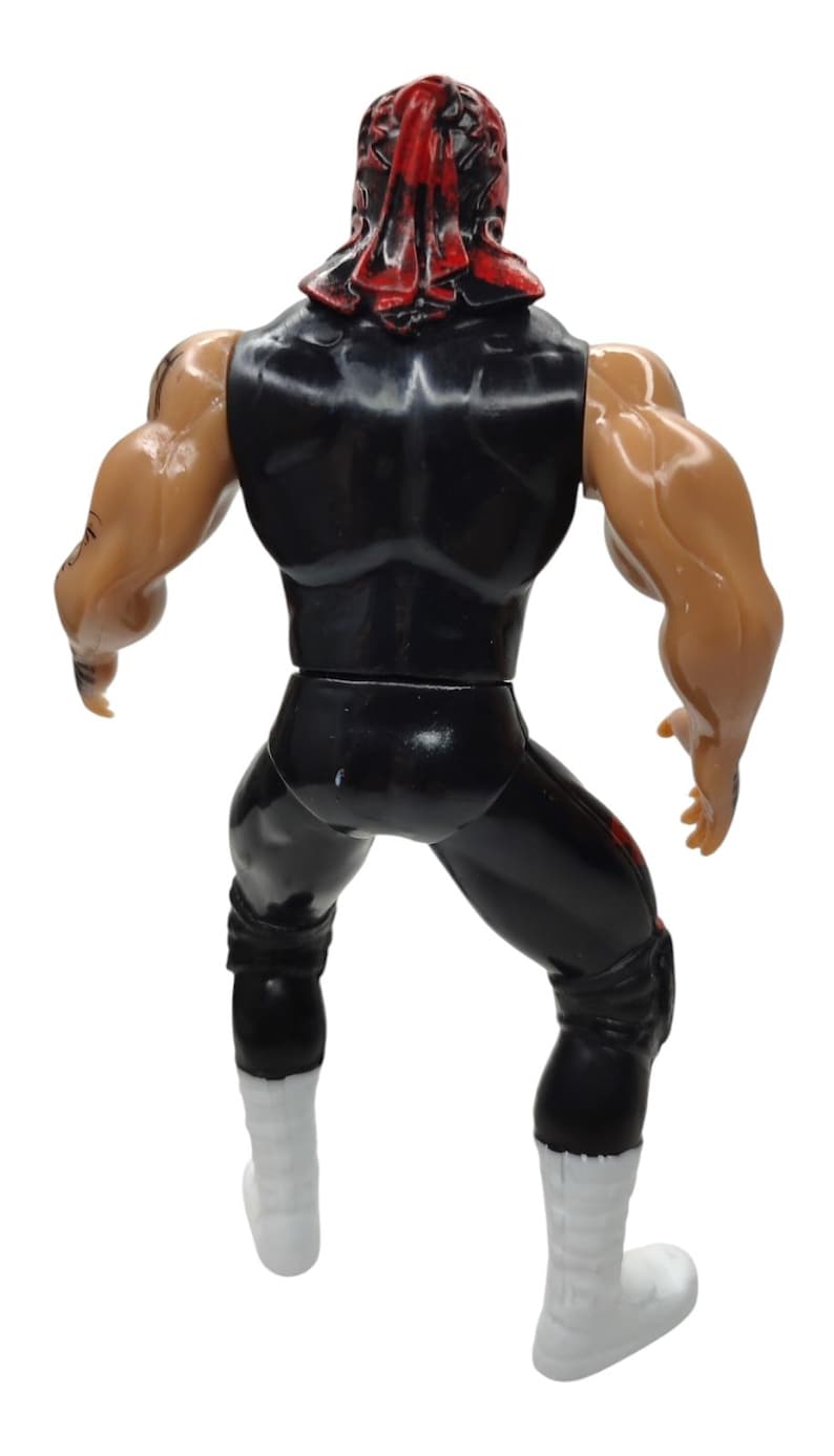 Puede incluir: Una figura de acci&oacute;n de pl&aacute;stico de un personaje musculoso, vista desde atr&aacute;s. La figura viste un atuendo negro con detalles rojos y botas blancas. Tambi&eacute;n es visible una cubierta para la cabeza roja y negra.