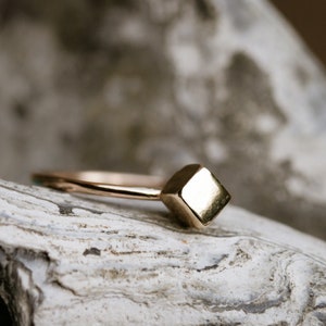 May include: A gold ring with a square-shaped band. The ring is sitting on a piece of rough, white rock.