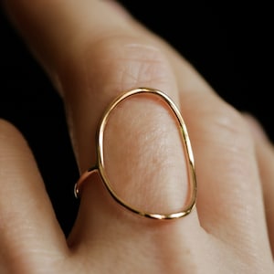 May include: A gold ring with a simple, organic oval shape. The ring is open and has a smooth, polished finish.