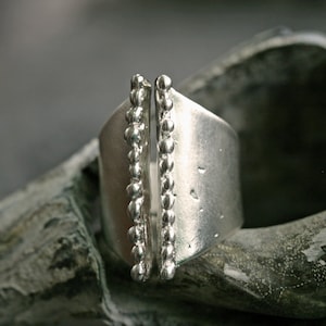 May include: A silver ring with a textured band and two rows of small beads on each side.