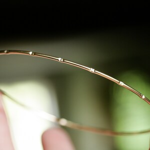 May include: A thin gold bangle bracelet with a simple design featuring small, evenly spaced, round accents.